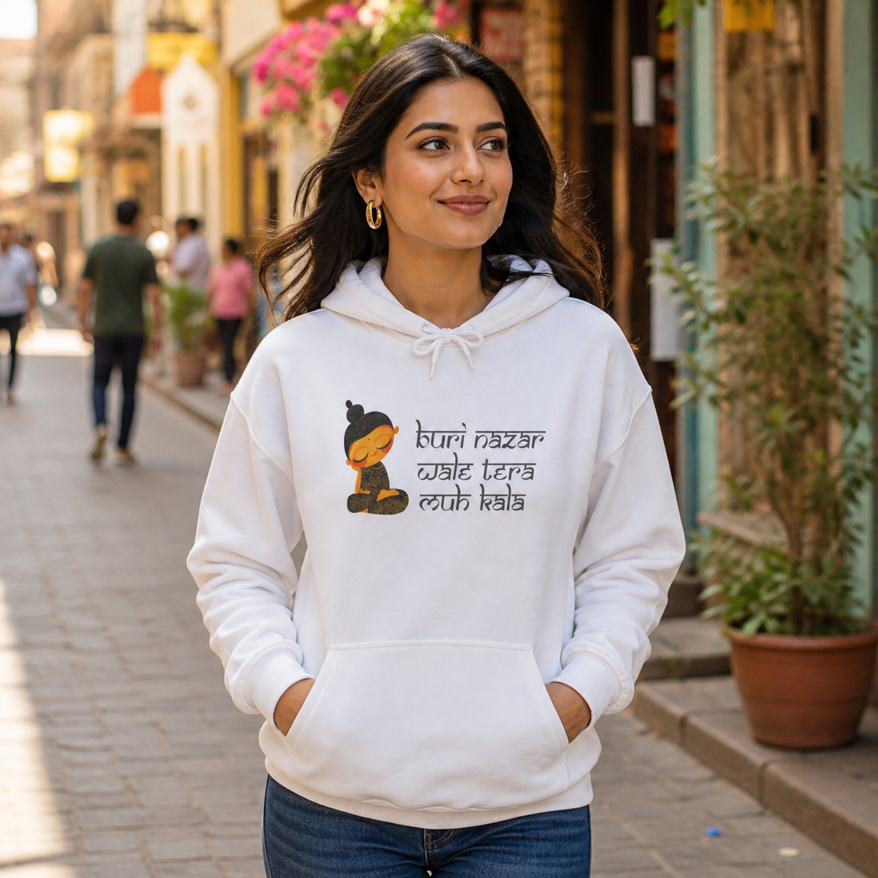 South Asian woman wearing a white Buri Nazar Wale graphic hoodie on an urban walkway