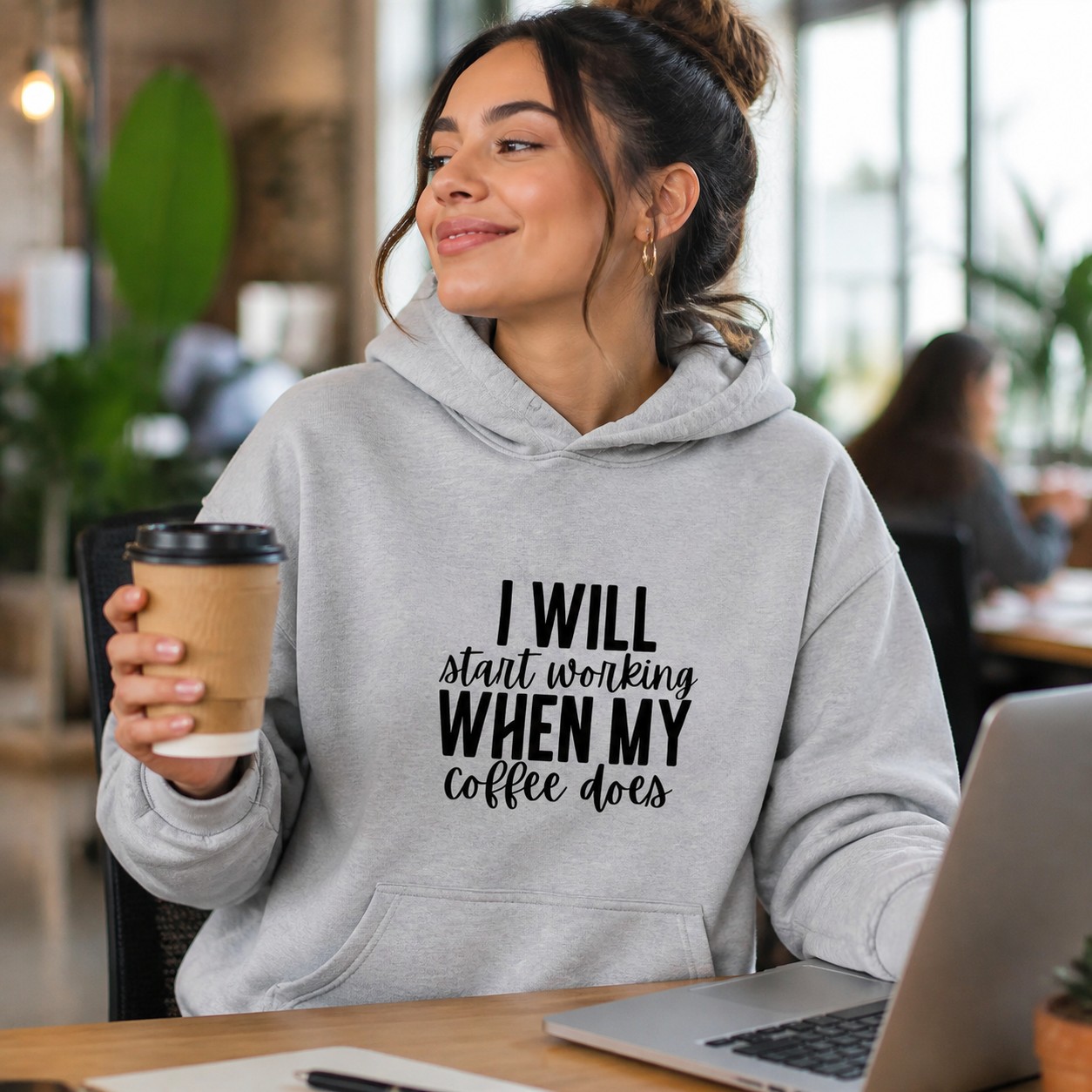 Woman wearing gray I Will Start Working When My Coffee Does hoodie in a coworking studio
