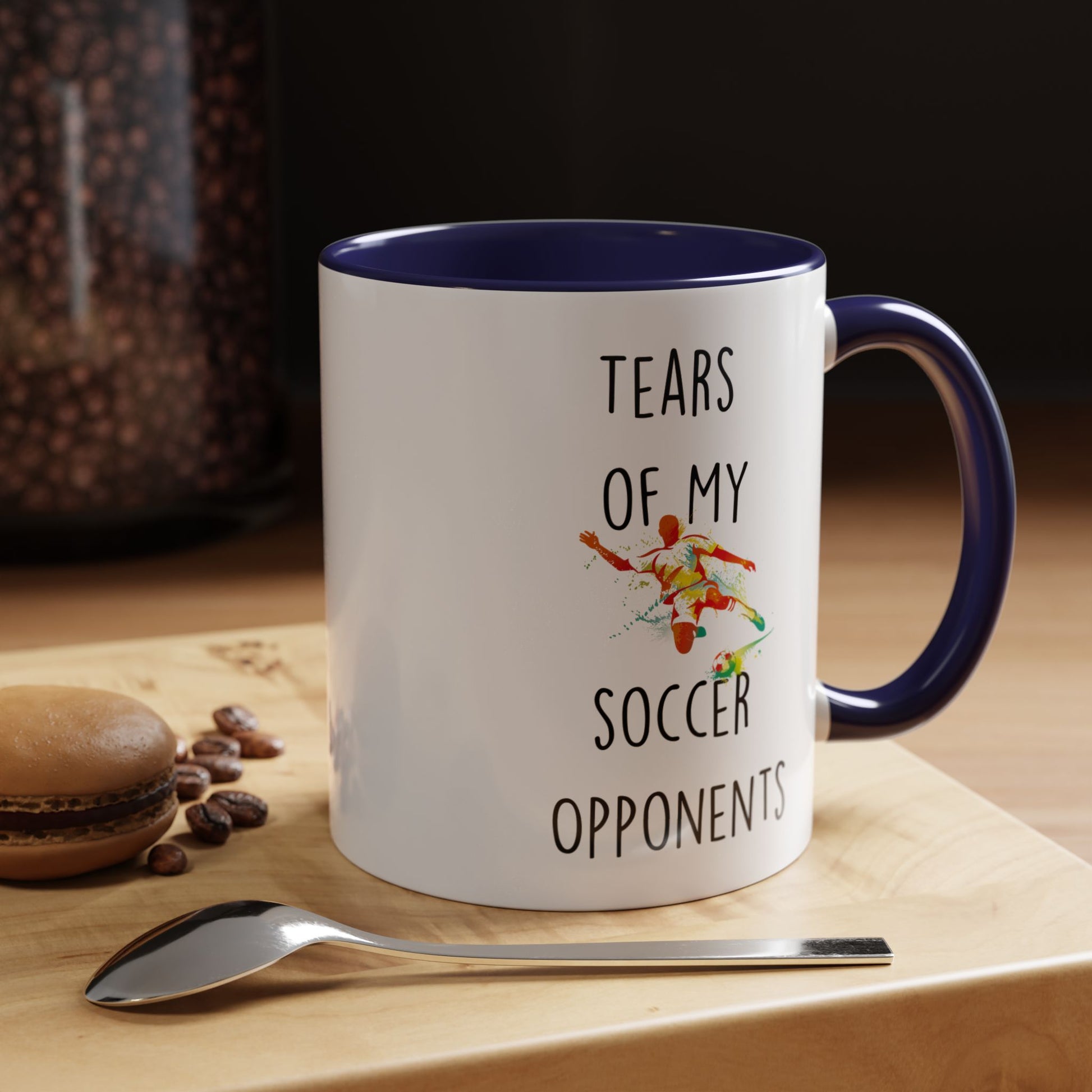 Personalized sarcastic coffee mug 'Tears Of My Soccer Opponents' next to a spoon and macaron on a wooden surface.