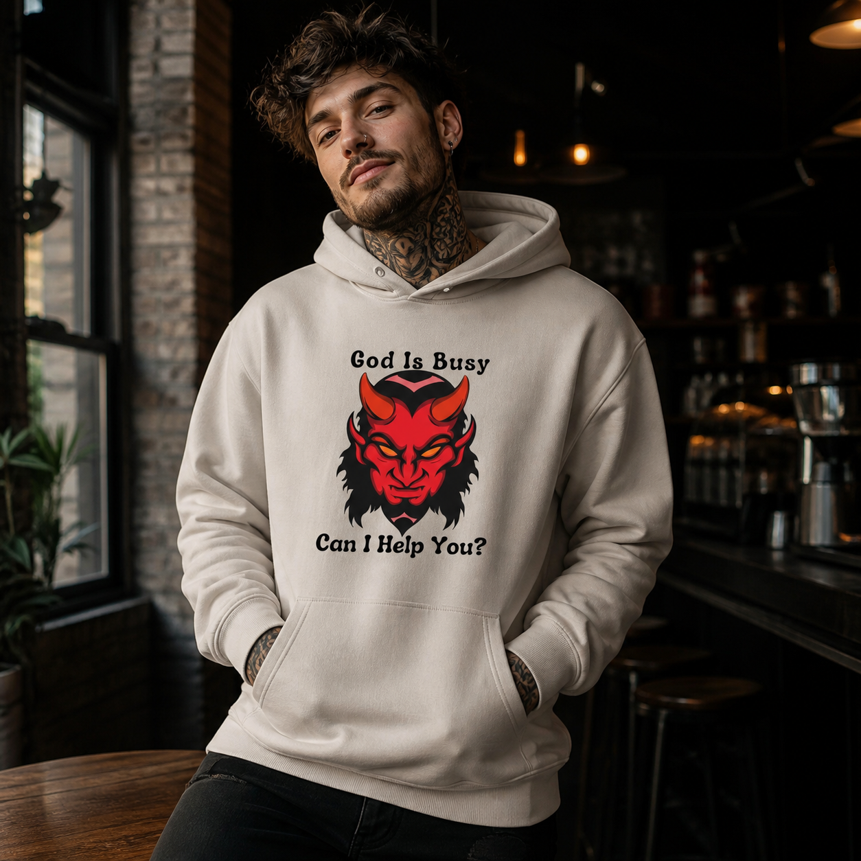 Young man wearing God Is Busy Can I Help You devil graphic hoodie in a coffeehouse
