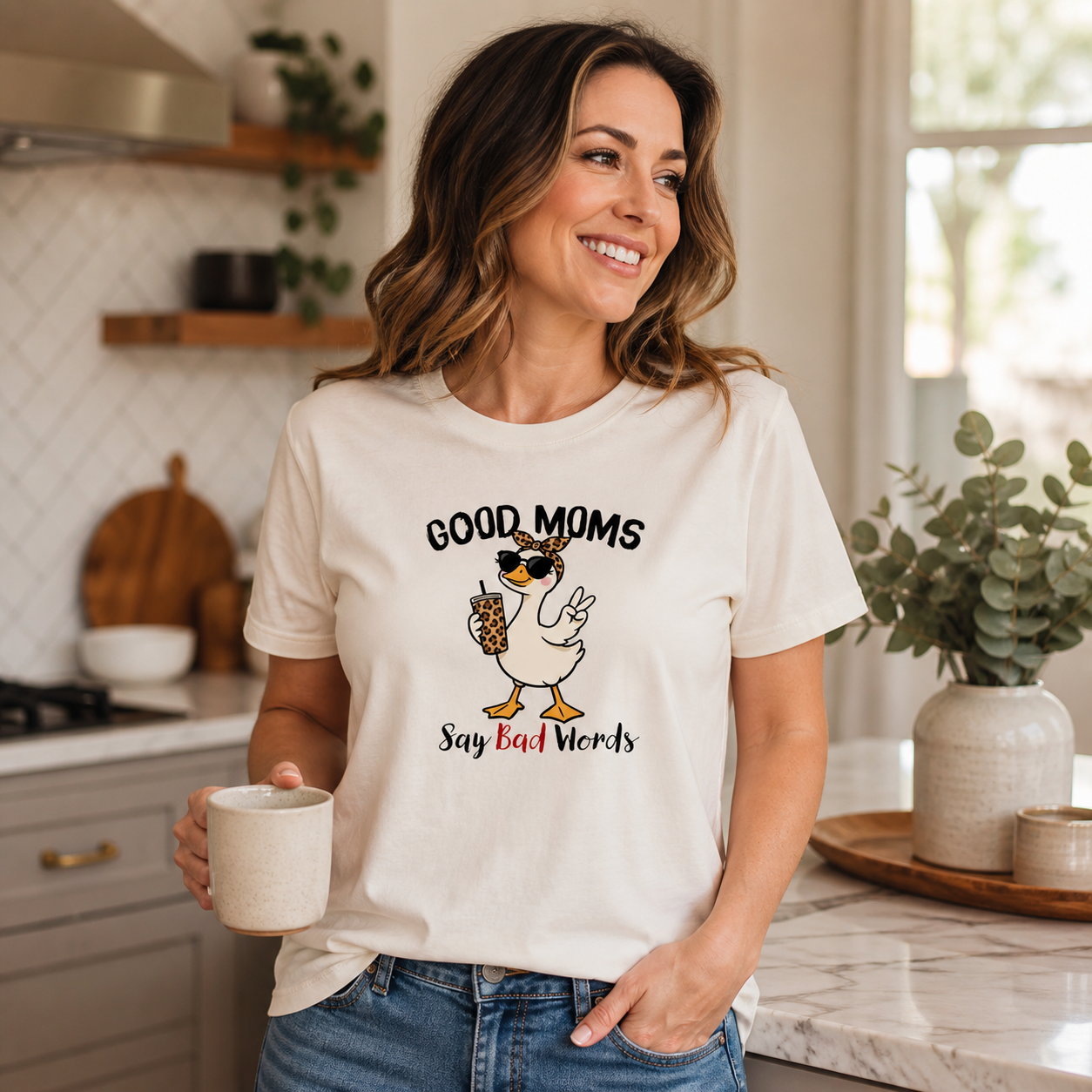 Mom wearing Good Moms Say Bad Words Mama Goose graphic T-shirt in a bright kitchen