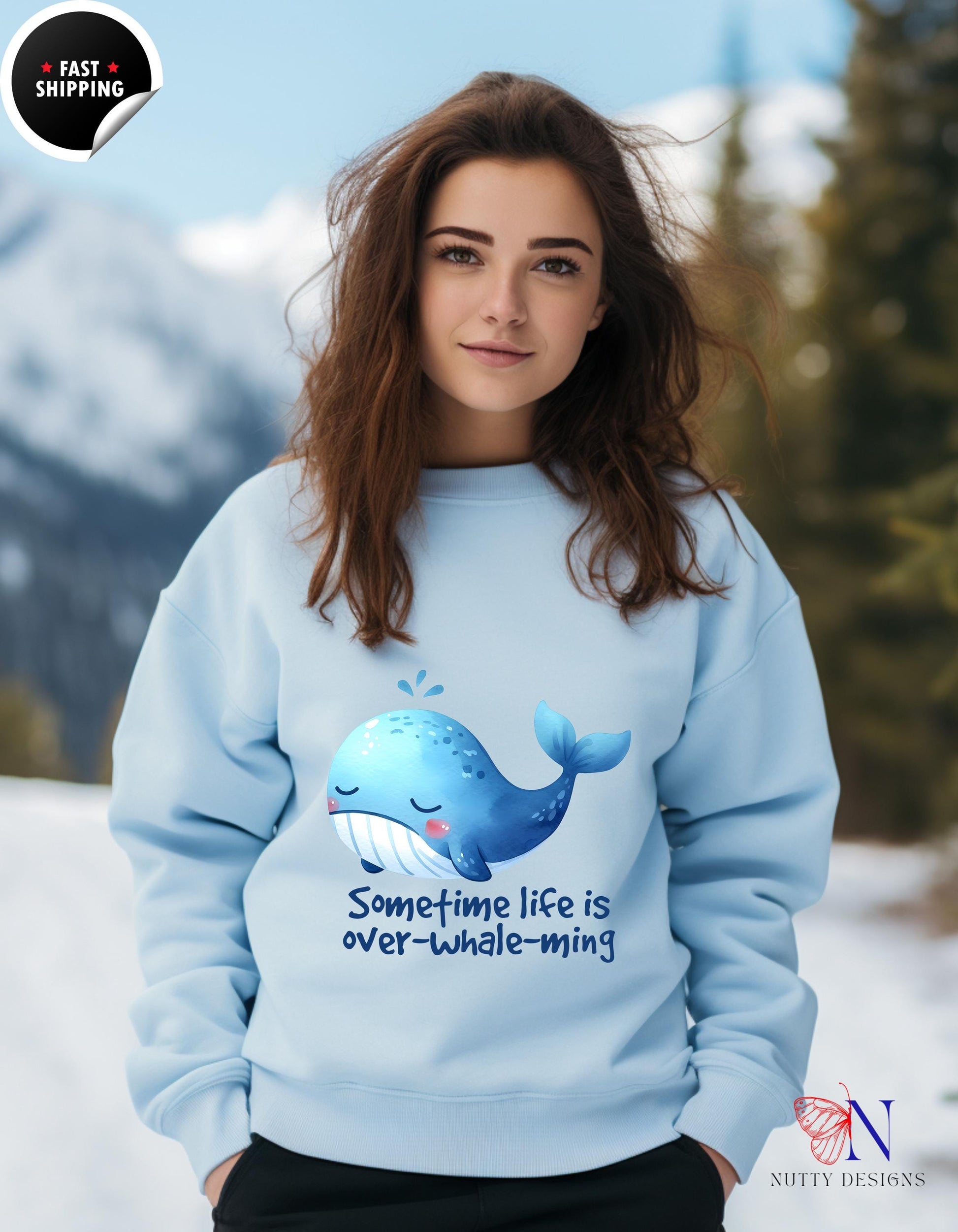 Woman wearing a blue sweatshirt with a whale graphic and the text 'Sometime life is over-whale-ming'.