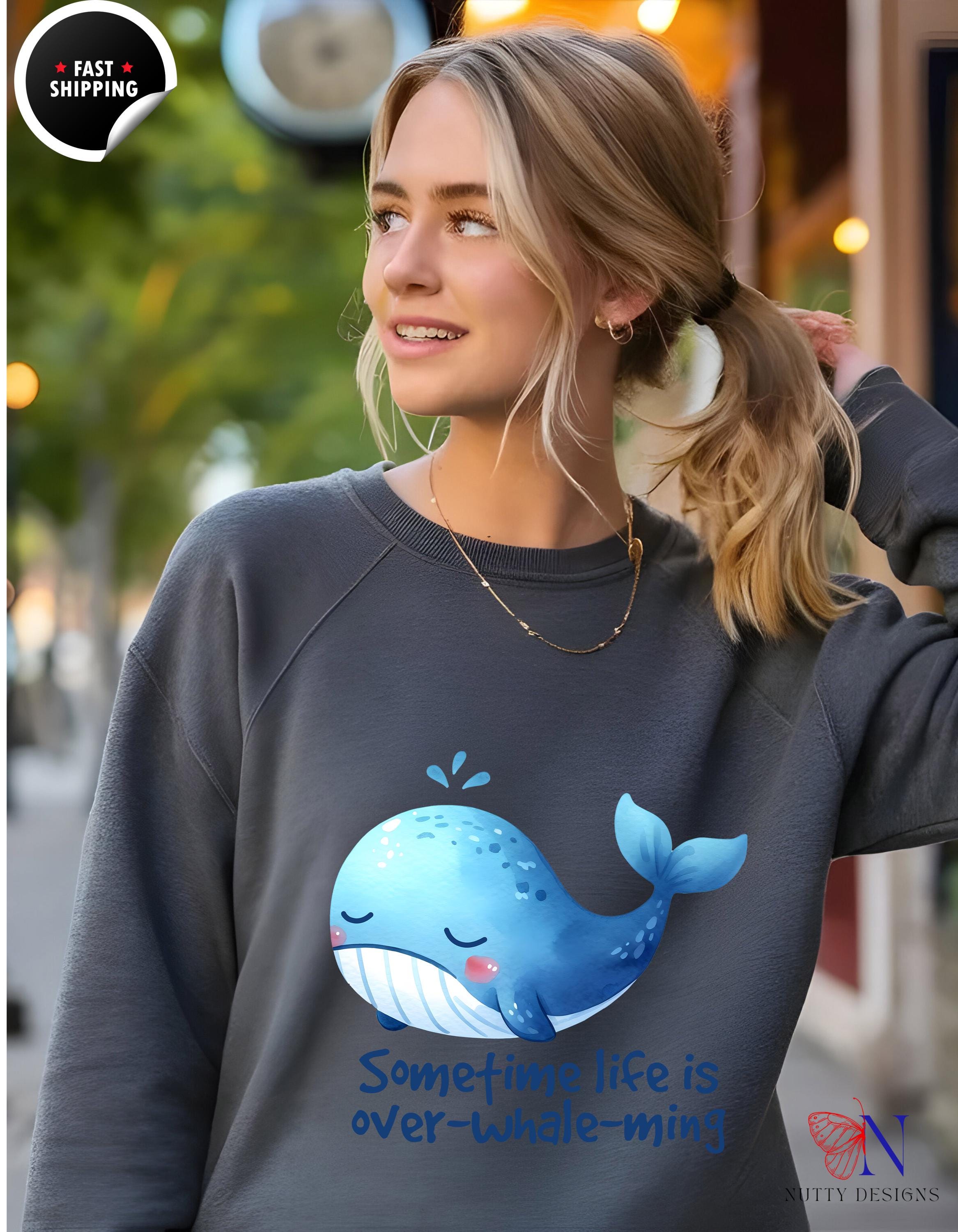 Woman wearing a grey sweatshirt with a cute whale graphic and the text 'Sometime life is over-Whale-ming' in blue.