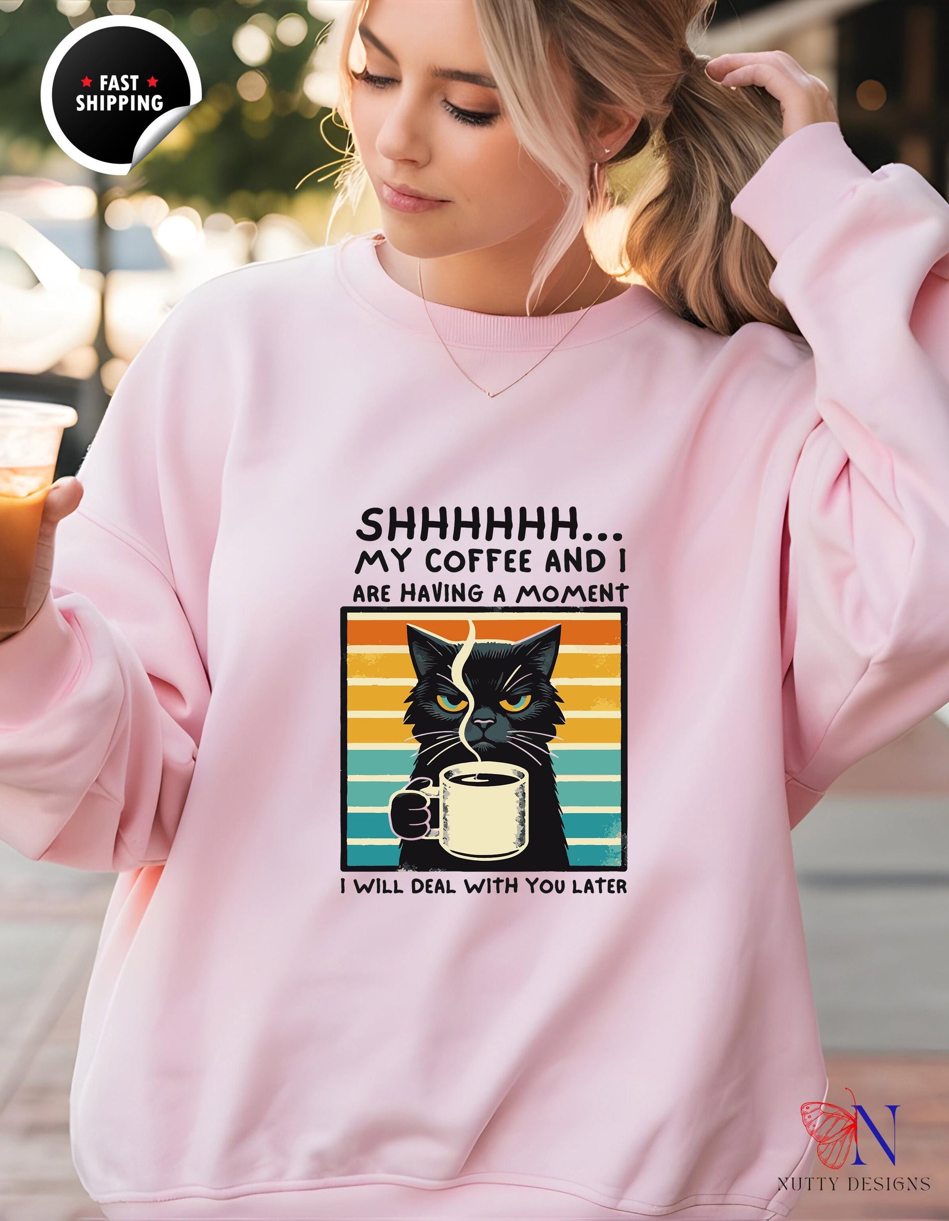 a woman wearing a sweatshirt with a black cat drinking coffee