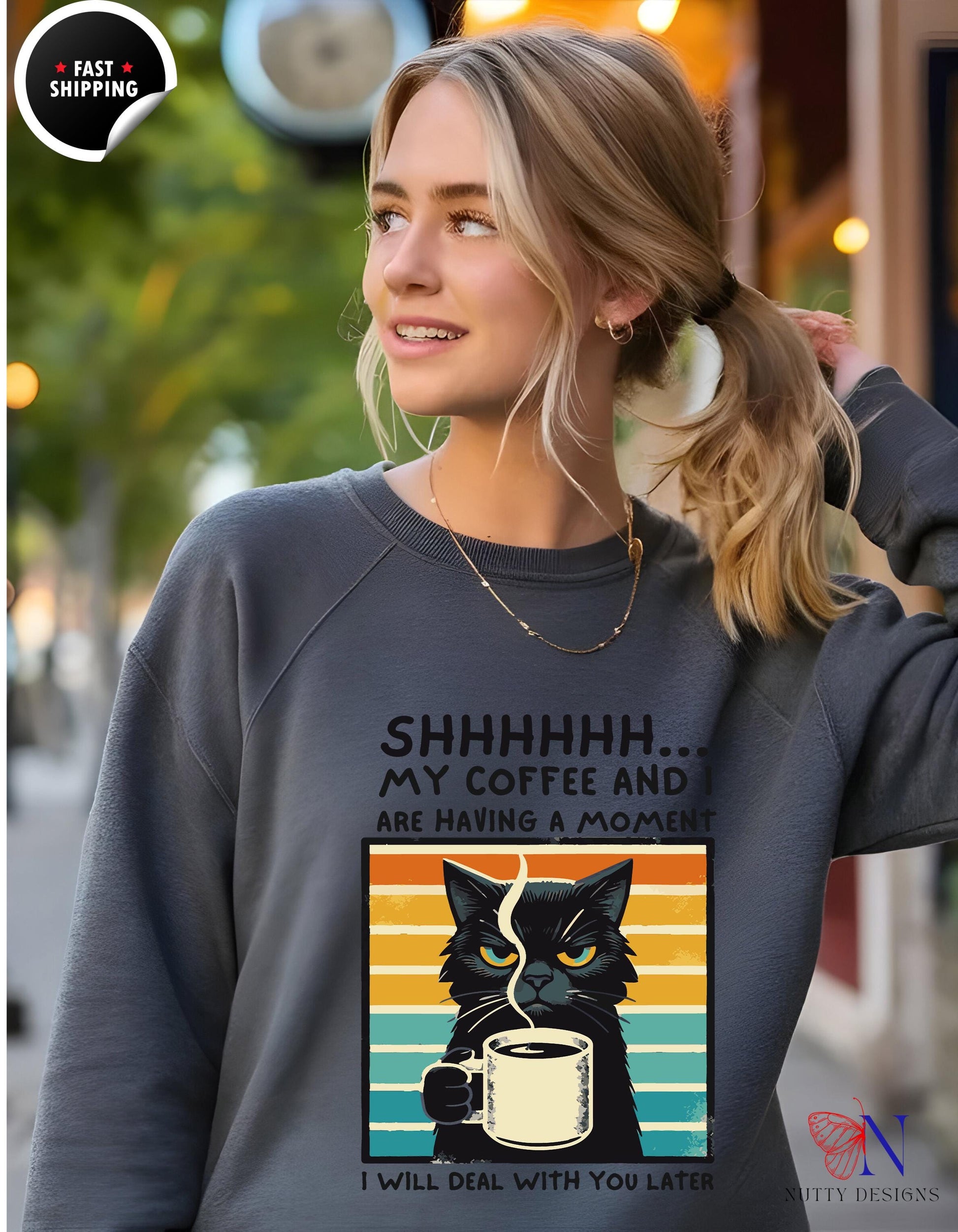 a woman wearing a sweatshirt with a black cat drinking coffee