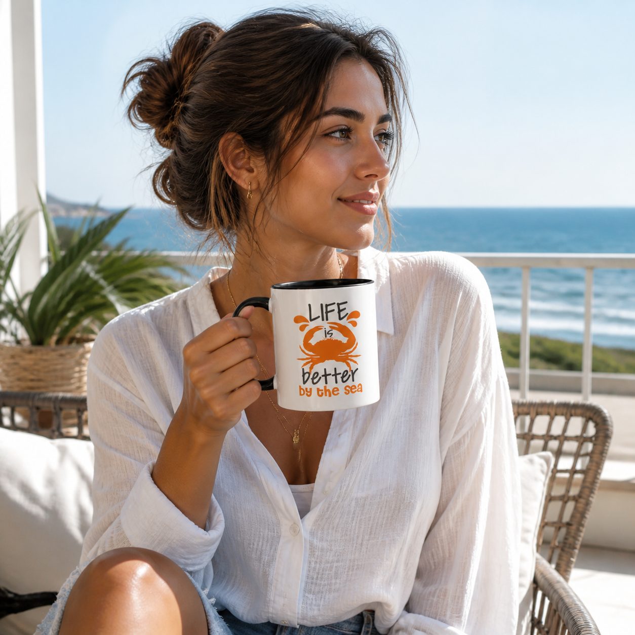 Woman holding black accent Life Is Better by the Sea crab coffee mug on a coastal balcony