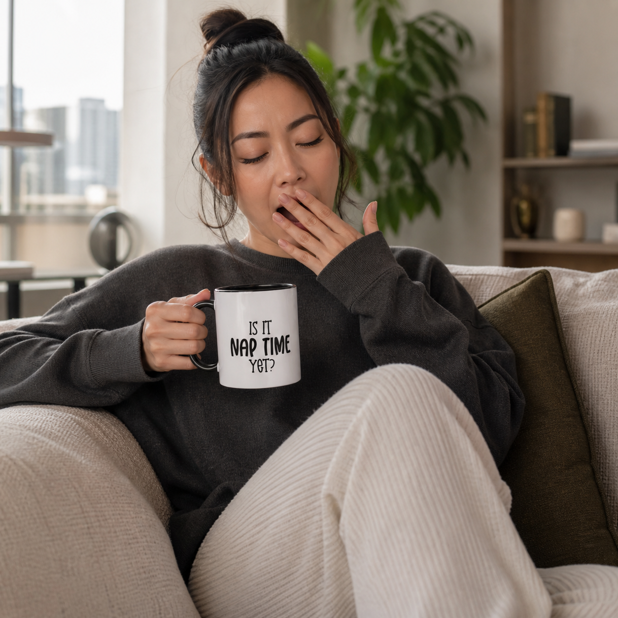 Young woman holding black accent Is It Nap Time Yet funny coffee mug on a sofa