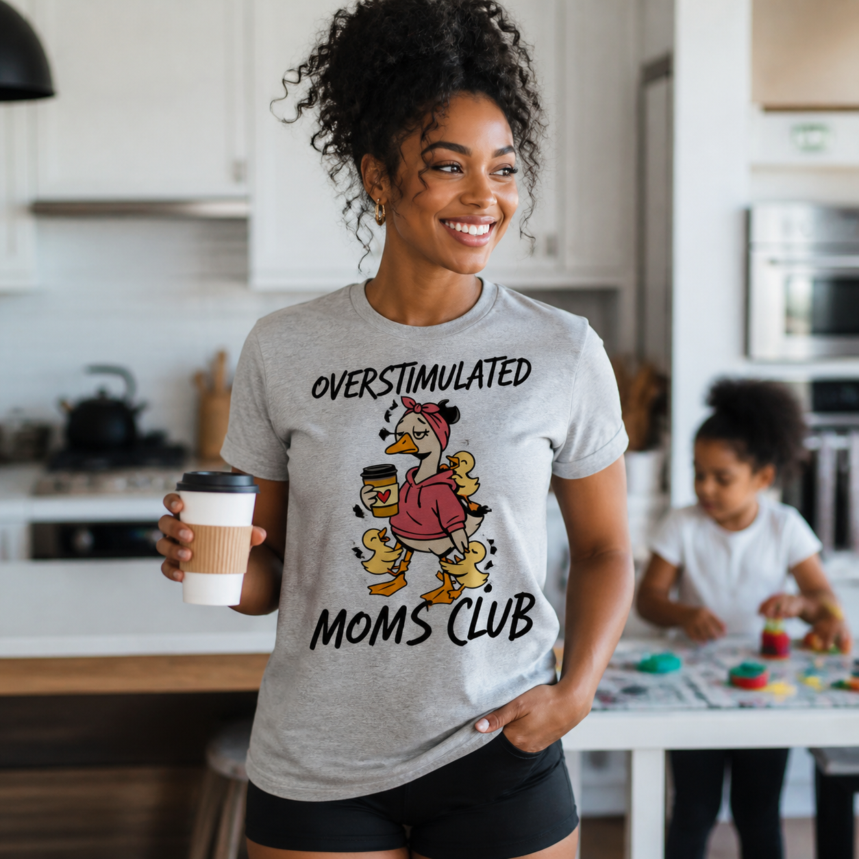 Young mother wearing Overstimulated Moms Club duck graphic T-shirt in a family kitchen