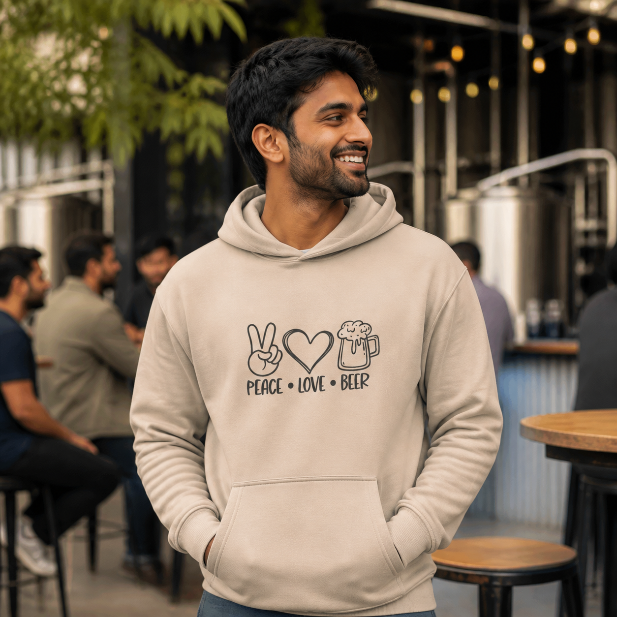Man wearing sand Peace Love Beer graphic hoodie at a brewery courtyard