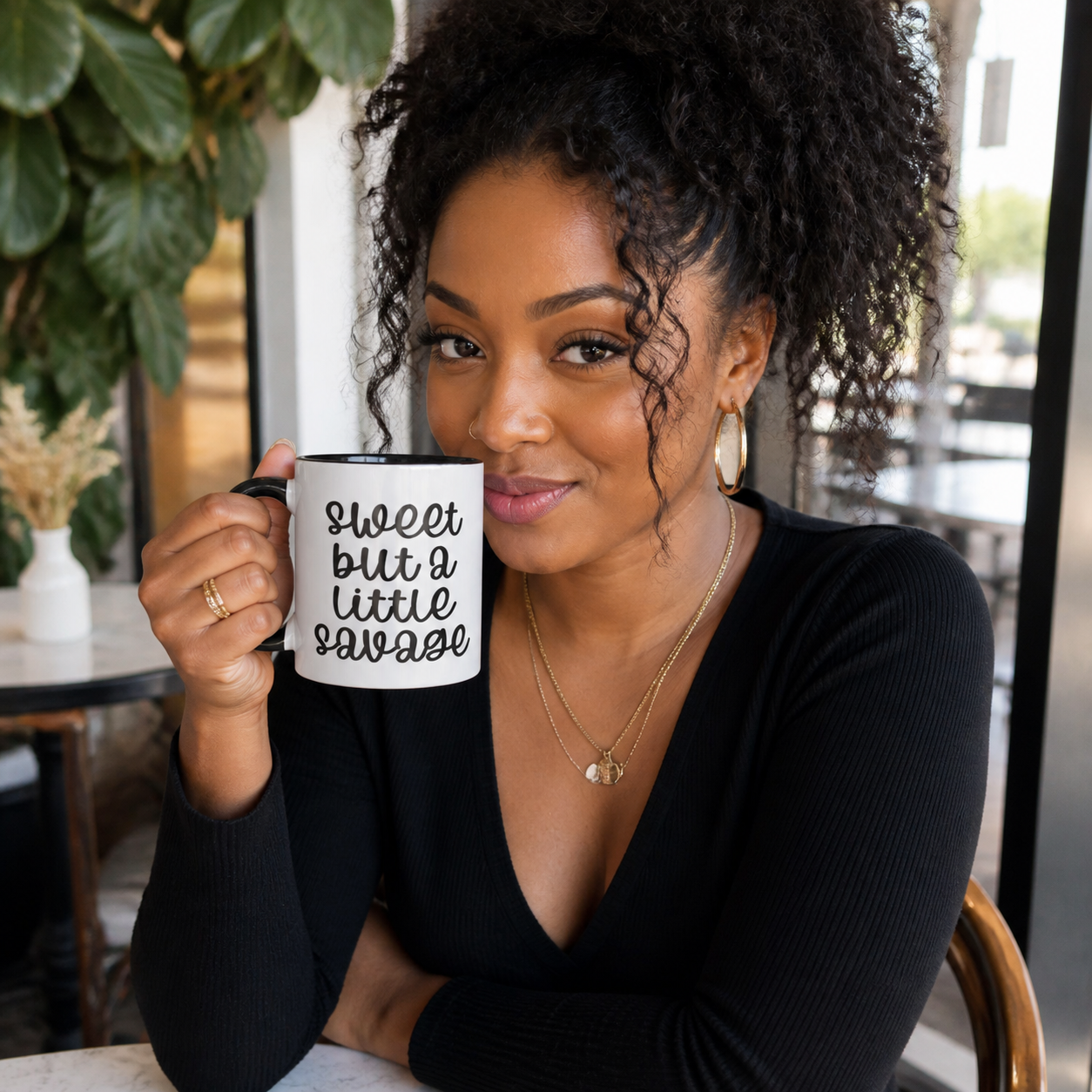Young woman holding black accent Sweet but a Little Savage coffee mug in a cafe