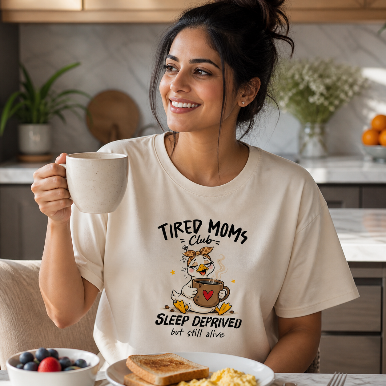Young mom wearing Tired Moms Club goose T-shirt at breakfast