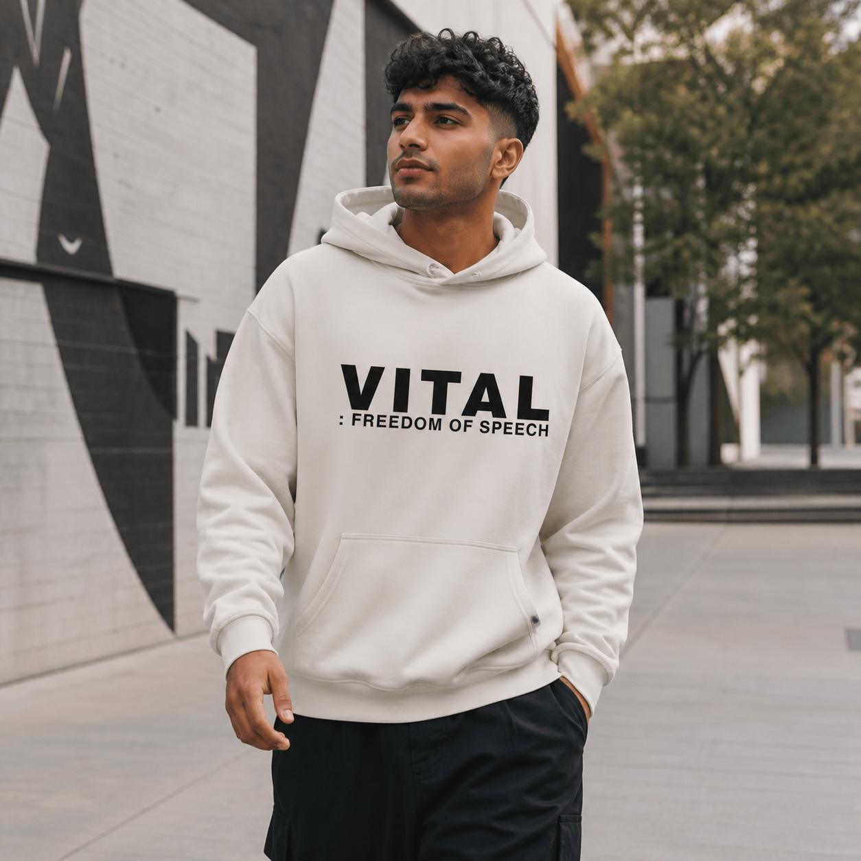Young man wearing stone Vital Freedom of Speech graphic hoodie in an urban arts district