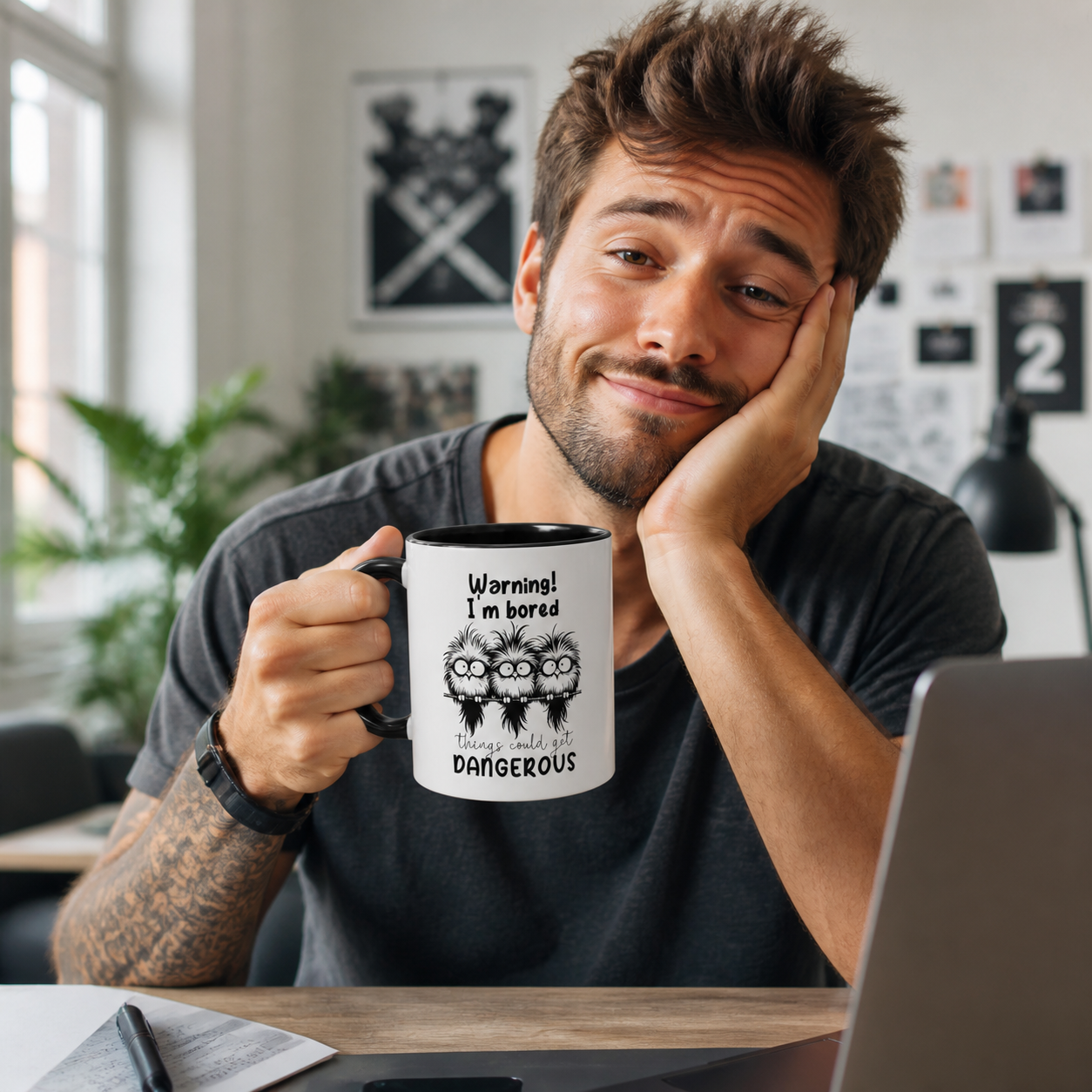 Young man holding black accent Warning I Am Bored owl coffee mug at a creative desk