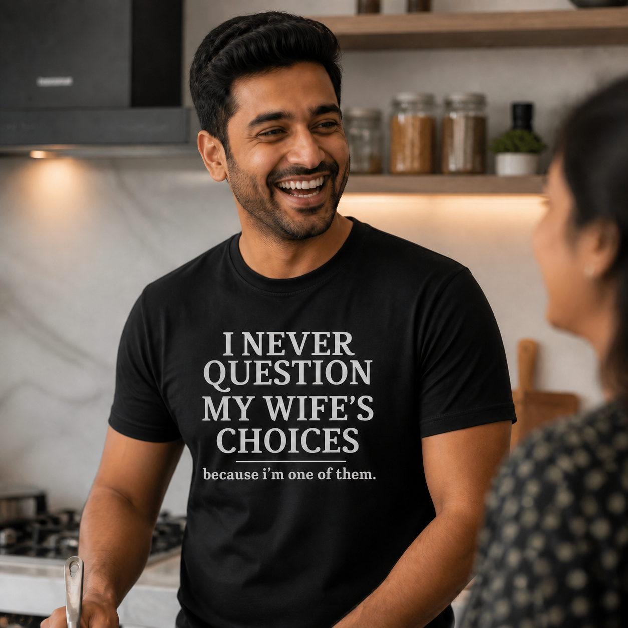 Husband wearing black I Never Question My Wife's Choices graphic T-shirt in a modern kitchen